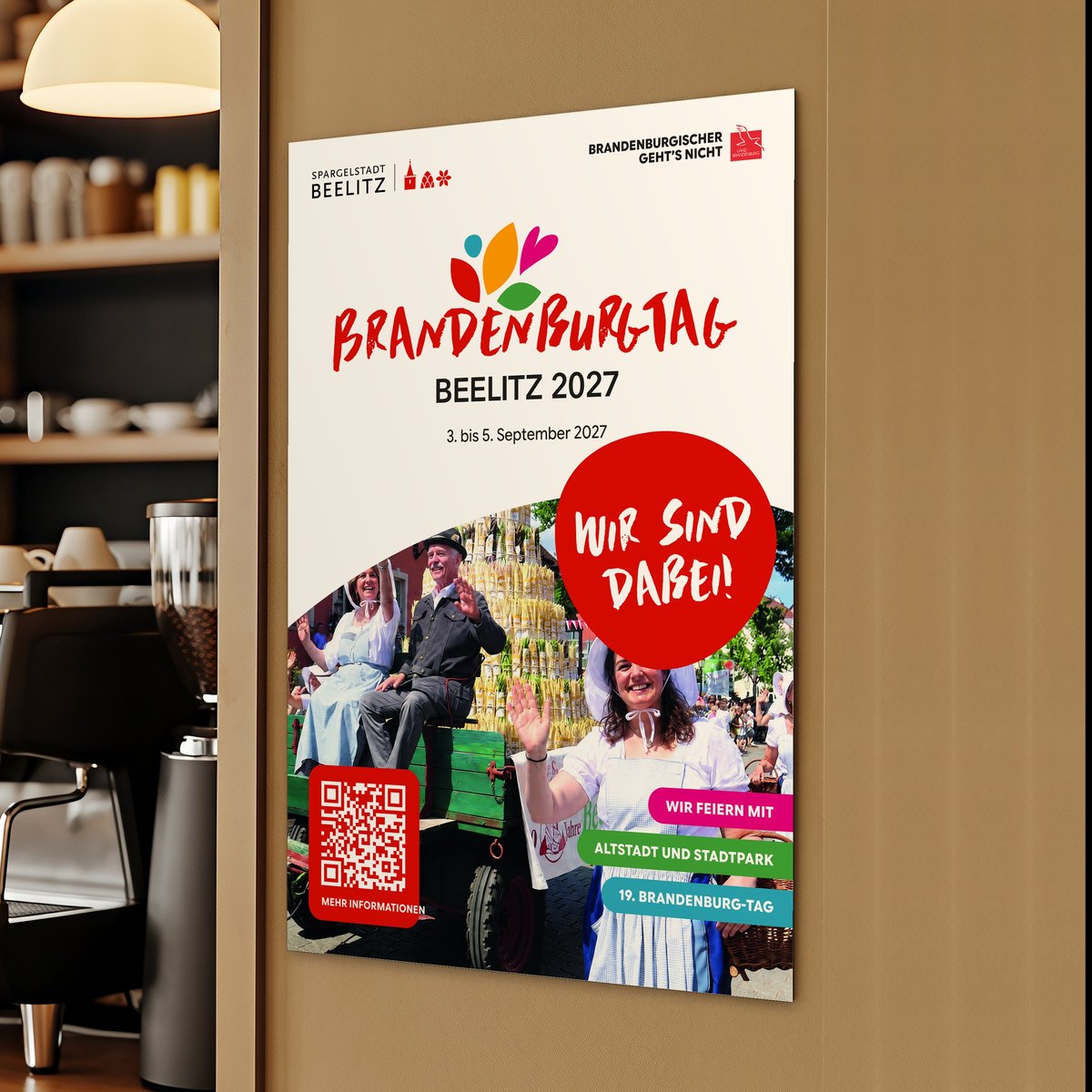 Das Poster „Wir sind dabei!“ zum Brandenburg-Tag 2027 hängt in einem Café neben der Theke an der Wand